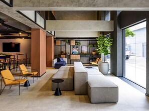 A modern lounge area with seating arrangements, a bar, and a large window providing a view of the street.