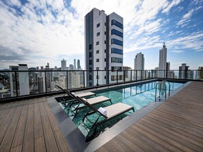 A rooftop pool with wooden decking, lounge chairs, and a city skyline view. - Ibis Balneario Camboriu (Balneário Camboriú)