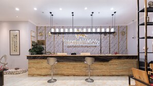 A hotel reception area with a marble counter, two bar stools, a chandelier, and a wall with framed artwork and a sign. - Qidajiudian (Deyang)
