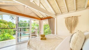 A bedroom with a bed, a view through a sliding door to a balcony, and a macrame wall hanging.