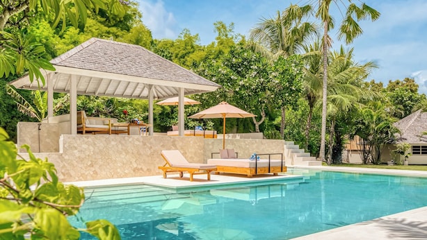A swimming pool with lounge chairs and umbrellas, surrounded by lush greenery and a covered seating area.