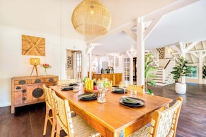 A spacious dining area with a wooden table set for six, surrounded by wicker chairs. A large woven light fixture hangs from the ceiling, and a wooden cabinet with drawers is visible to the left. - Spacious 2 Villas combined, 9 bedrooms, 2 pools (Kabupaten Badung)