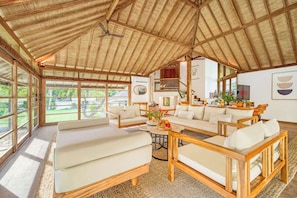 A spacious living area with a high ceiling, large windows, and a view of the outdoors.