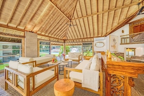 A spacious room with a high ceiling, wooden furniture, and large windows offering a view of the outdoors.