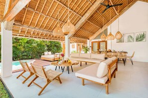 A spacious indoor area with a high ceiling, wicker furniture, and a dining area with a view of lush greenery. - Villa Indigo - 5-BDR, huge pool and lush garden (Kecamatan Kuta)