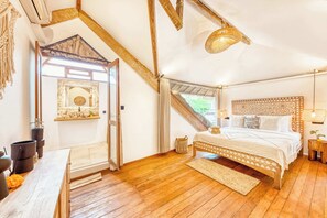 A cozy bedroom with a wooden ceiling, a bed with patterned bedding, a small bedside table, and a window with curtains. - Villa Indigo - 5-BDR, huge pool and lush garden (Kecamatan Kuta)