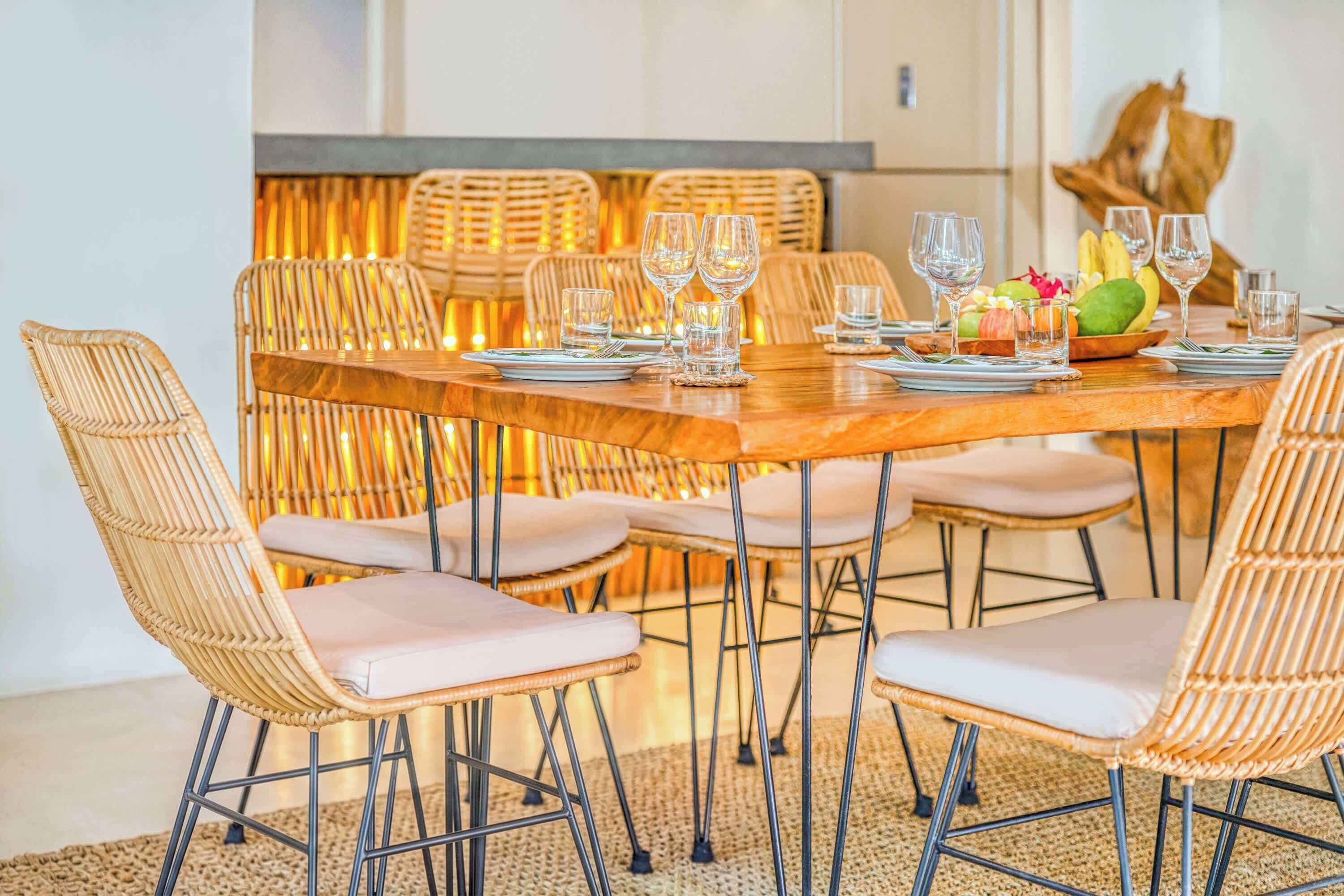 A dining area with wicker chairs, a wooden table, and a fruit bowl.