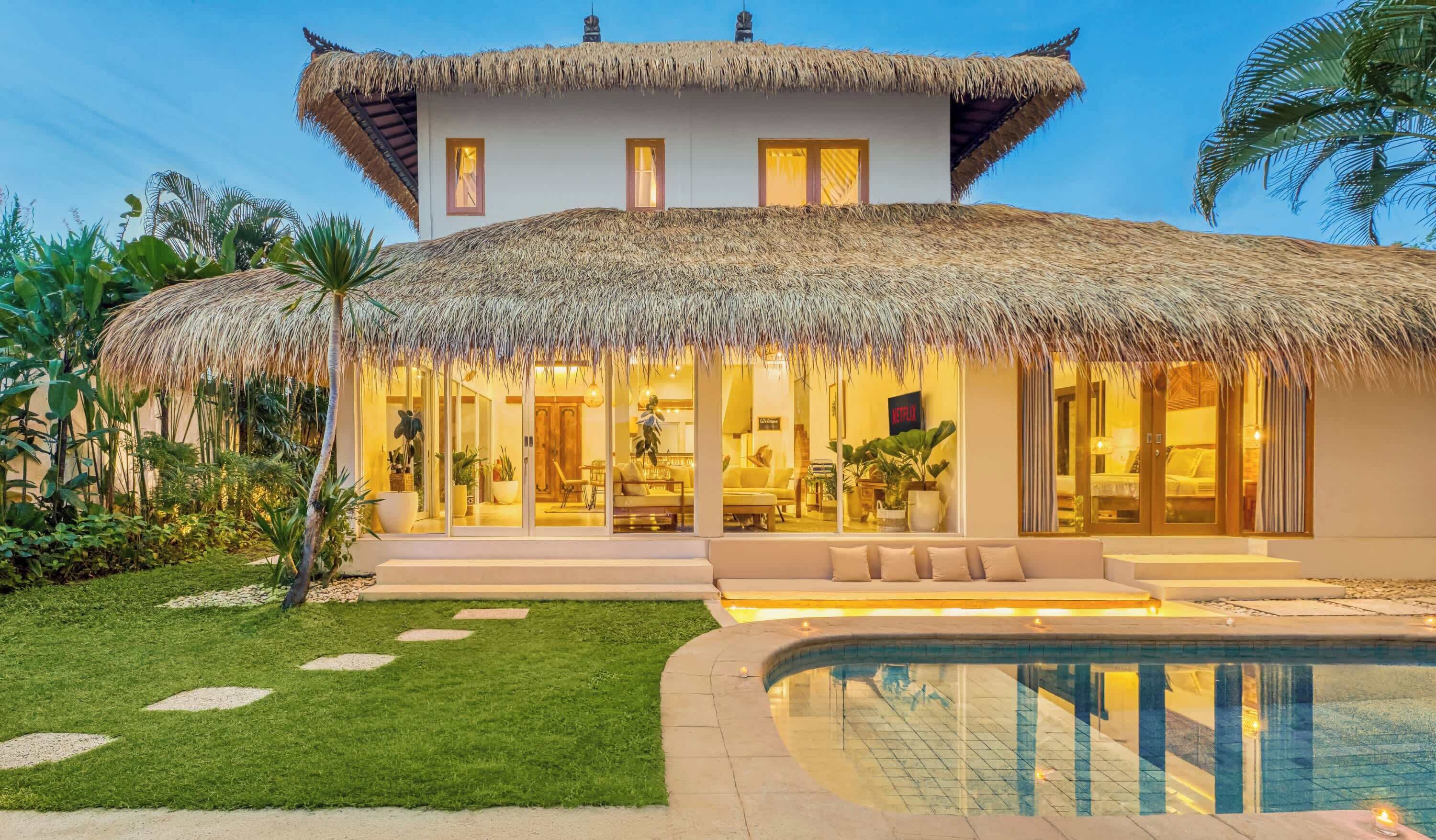 A modern house with a thatched roof, a swimming pool, and a well-maintained garden.