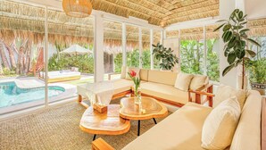 A spacious room with a large glass wall, a pool, and a thatched roof ceiling.
