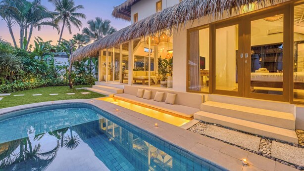 A modern resort with a pool, outdoor seating, and a thatched-roof structure.