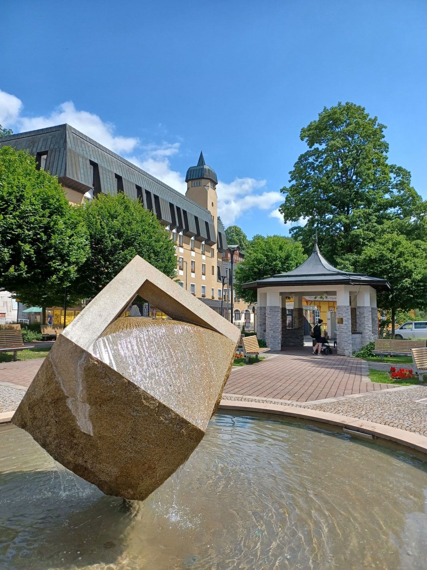 A public square with a fountain, a gazebo, and a building with a tower.