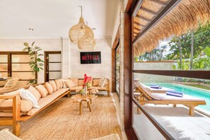 A spacious living area with a sofa, a coffee table, and a TV screen displaying 'NETFLIX'. - Villa Aurora - 6BDR, near beach, big pool & garden (Kuta)