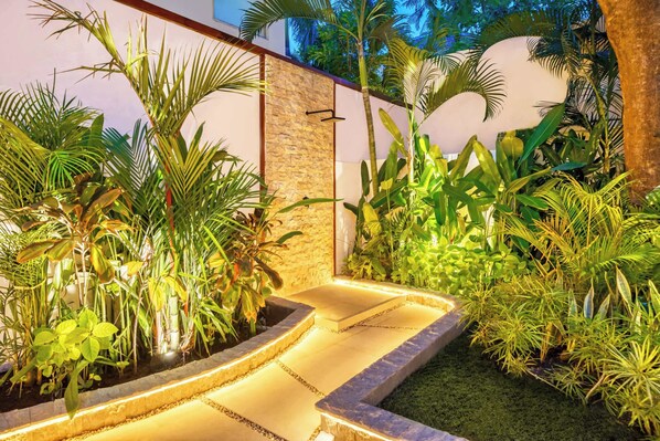 A landscaped garden with a stone wall, various tropical plants, and a paved pathway.