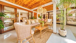 Un salón espacioso con muebles de mimbre, techo de madera y grandes ventanales.