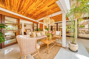 A spacious living area with wicker furniture, a wooden ceiling, and large windows.