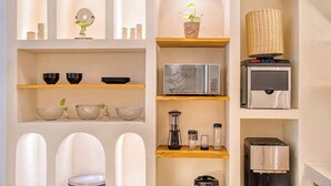 Una cocina con microondas, licuadora y cafetera sobre estantes, una cesta colgante con plantas y una pared decorativa con nichos abovedados.