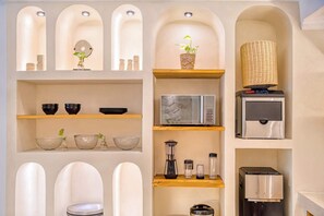 A kitchen with a microwave, blender, and coffee machine on shelves, a hanging basket with plants, and a decorative wall with arched niches.