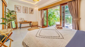 A bedroom with a bed, a desk, a chair, a large window, and a potted plant. - Villa Florence - 3BDR Luxury Bali Oasis (Kecamatan Kuta Selatan)