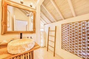 A bathroom with a wooden vanity, a large mirror, a sink, and a decorative wall panel.