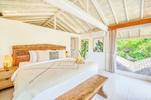 Un dormitorio con una cama grande, cabecera de madera, mesitas de noche, un banco y vistas a zonas verdes.