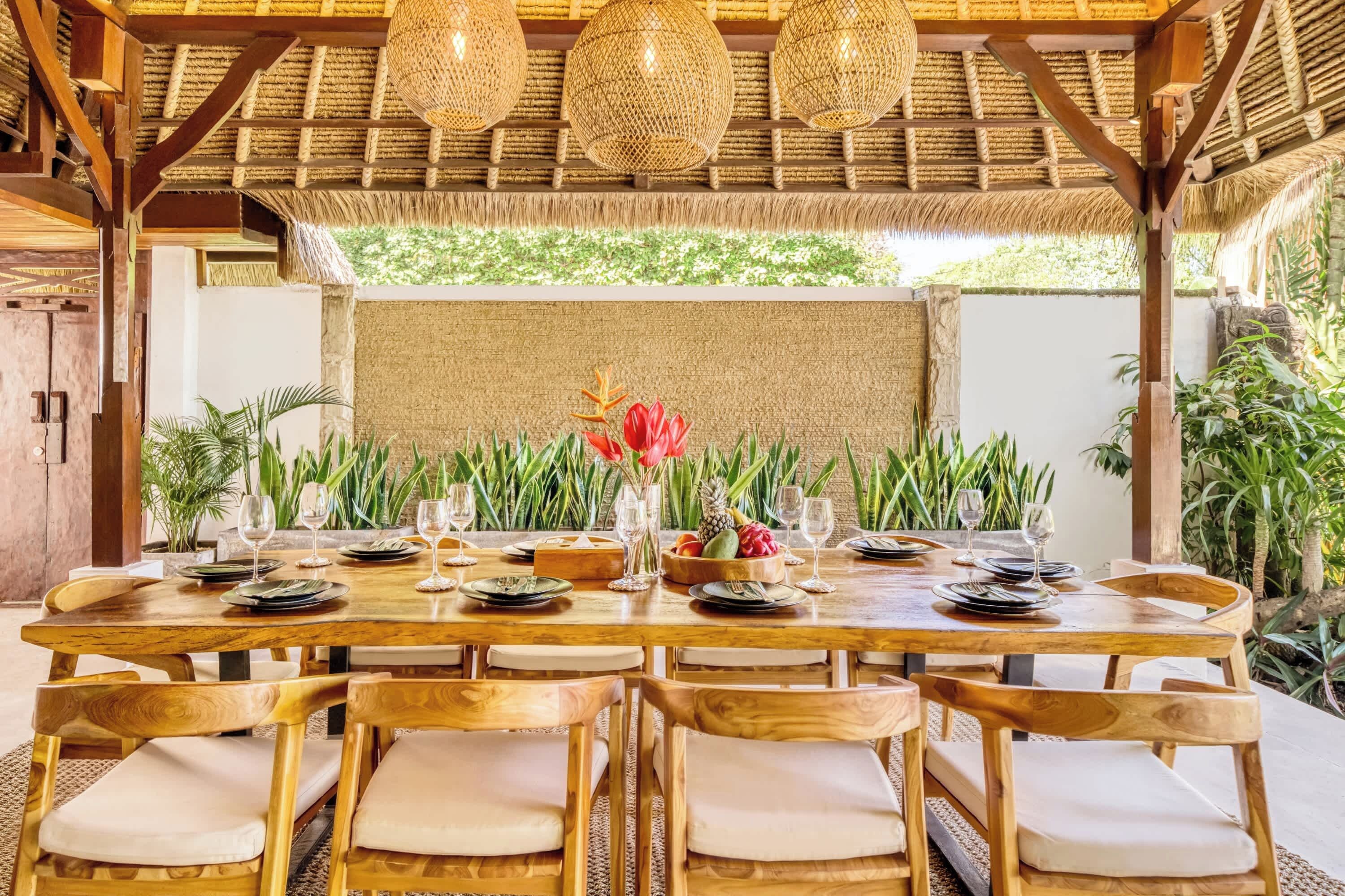 Une table de salle à manger en bois, mise avec des assiettes, des verres et un centre de table composé de fruits et de fleurs.