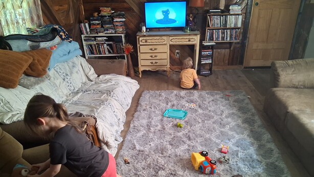 Una sala de estar acogedora con un sofá, una mesita de centro y una alfombra. Hay niños jugando con juguetes, y un televisor enciendendo de fondo.