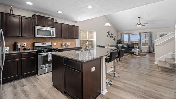 A modern kitchen with dark wood cabinets, a stainless steel microwave, and a granite countertop.