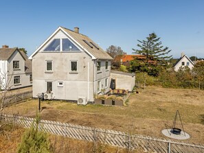 A two-story house with a sloped roof, a small front porch with outdoor seating, and a fenced yard.
