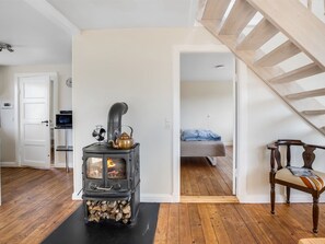 Une pièce avec un poêle à bois, un lit, une chaise et un escalier.