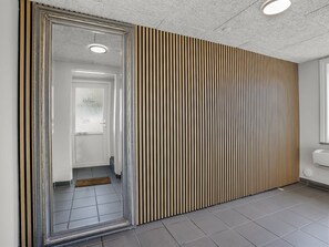 Un couloir avec un mur recouvert de miroirs, une porte ornée d’une pancarte « Bienvenue » et un design moderne à panneaux verticaux.