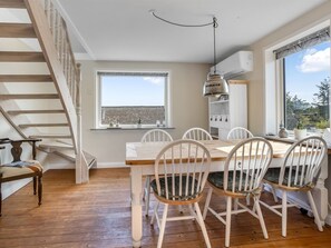 Un comedor con mesa y sillas de madera, una escalera y un ventanal con vistas.