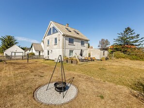 Une maison à deux étages avec un grand jardin, un barbecue et une zone délimitée par une clôture.