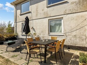 Une terrasse avec une table et des chaises, un transat et un petit coin jardin.