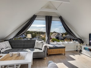 Une chambre de style loft moderne, dotée d’une grande fenêtre, d’un canapé gris, d’une petite table et d’un téléviseur.