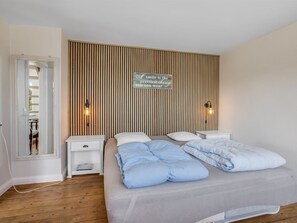 Une chambre à coucher comprenant un lit, deux tables de chevet, une lampe fixée au mur et un panneau décoratif.