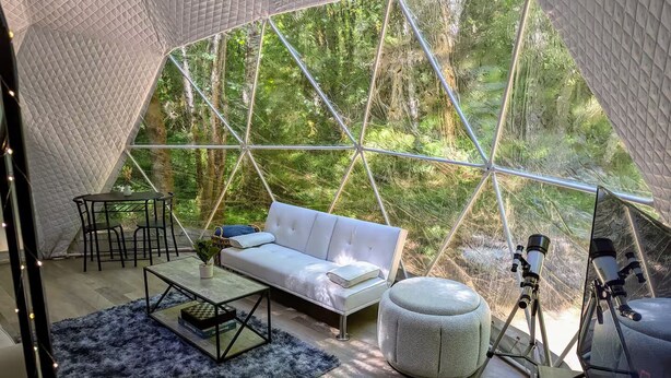 Un interior acogedor y moderno con un sofá blanco, un reposapiés redondo pequeño, una mesita de centro y un telescopio.