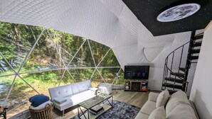 Un salón moderno y espacioso con techo de vidrio, un sofá, una mesa de centro y un televisor.