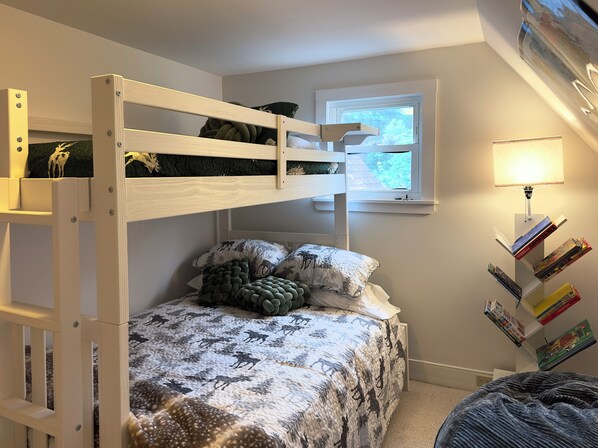 Un lit superposé avec une fenêtre au-dessus, une lampe de chevet et une bibliothèque remplie de livres.