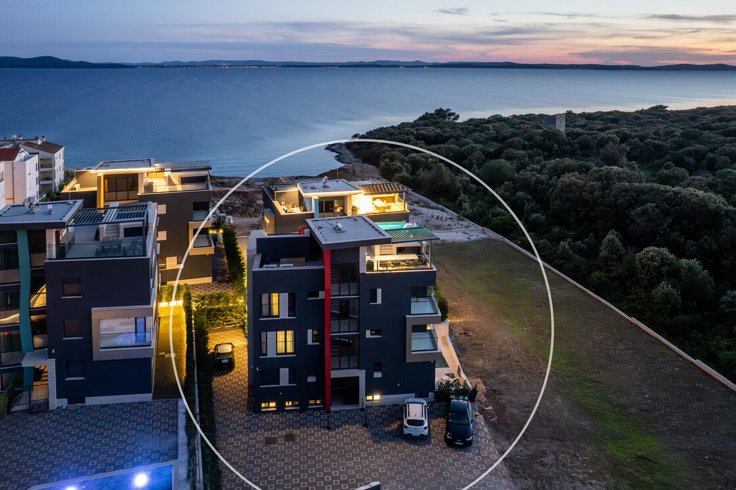 A modern apartment complex with multiple buildings, a rooftop pool, and a view of the sea.