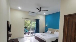 A hotel room with a bed, a ceiling fan, an air conditioning unit, a TV, a small table, and a sliding glass door leading to an outdoor area. - Agusto's Beach Stay (Calangute)