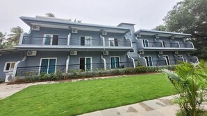 A two-story residential building with a flat roof, multiple air conditioning units, and a well-maintained lawn in the foreground. - Agusto's Beach Stay (Calangute)