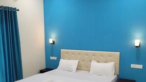 A bedroom with a large bed, two bedside tables, and a blue accent wall. - Agusto's Beach Stay (Calangute)