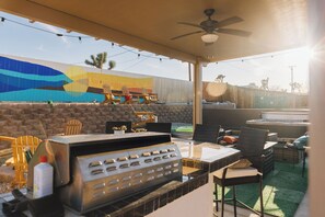 An outdoor patio with a grill, chairs, and a mural on the wall. - Desert Zen: NEW Heated Pool, Hot Tub, Fire Pit, Game Room, Views & More! (Joshua Tree)