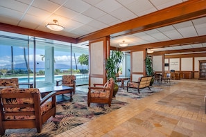 A spacious lobby with a pool view, wooden furniture, and a tropical-themed carpet.