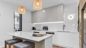 Una cocina moderna con armarios blancos, una isla central con taburetes, iluminación colgante y horno integrado.