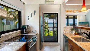 A modern kitchen with a view of the beach, a coffee machine, and a sign that reads 'THE BEACH'.