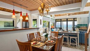 A modern kitchen with wooden ceiling beams, a dining area with a glass table, and a view of the sea.