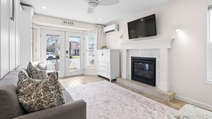 A modern living room with a fireplace, a ceiling fan, and a TV mounted above it.