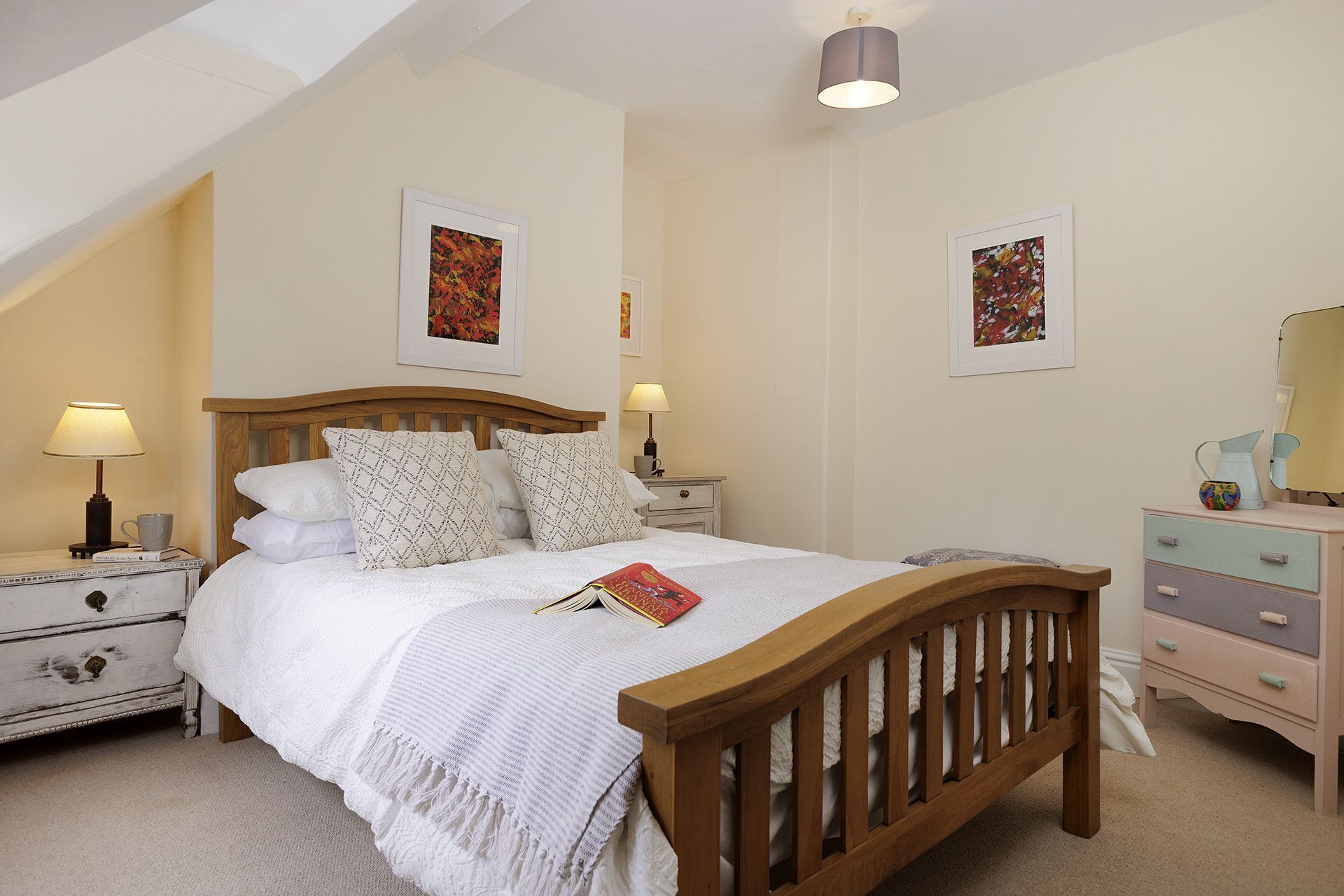 A bedroom with a wooden bed, white bedding, two bedside tables with lamps, and two framed pictures on the walls.