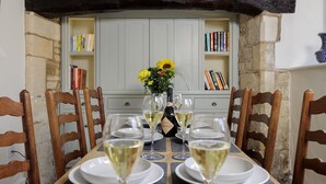 Ein Esstisch ist mit weißen Tellern und Gläsern, einer Prosecco-Flasche und einer Blumenvase gedeckt.